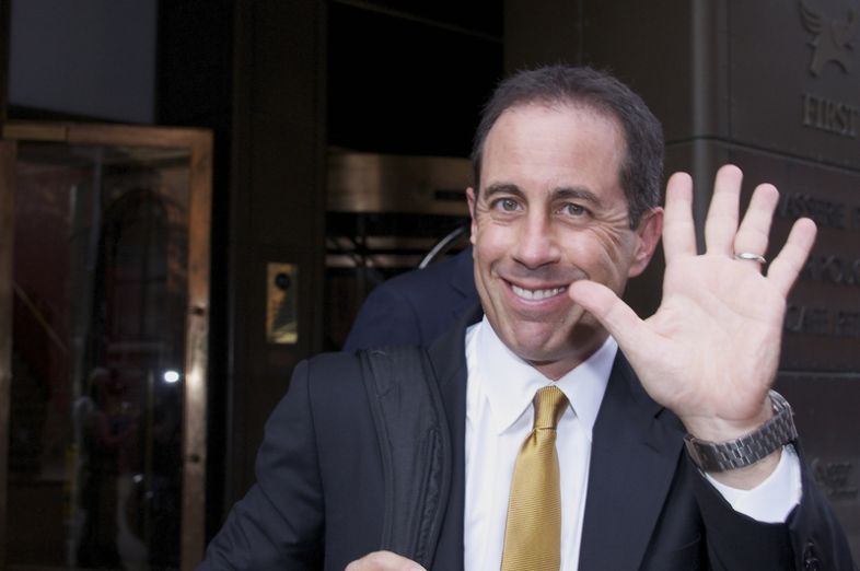 Jerry Seinfeld smiling and waving as he leaves his hotel